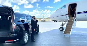 Professional chauffeur in a black suit standing by a luxury SUV on the tarmac next to a private jet, providing Smyrna airport limo service for a seamless and reliable executive transfer.